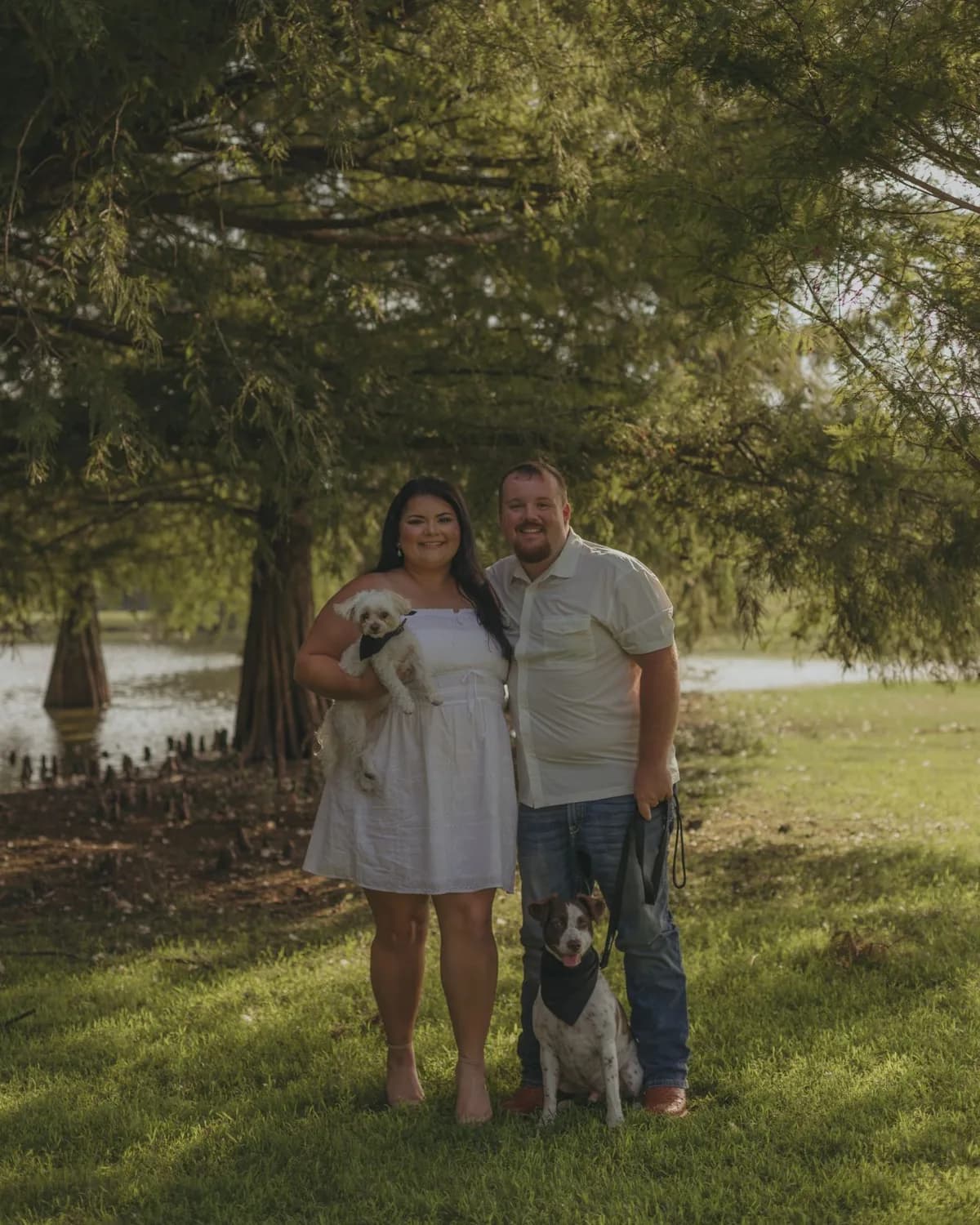 The owner of Gulf South Stump Grinding with two dogs, standing under cypress trees by a lake